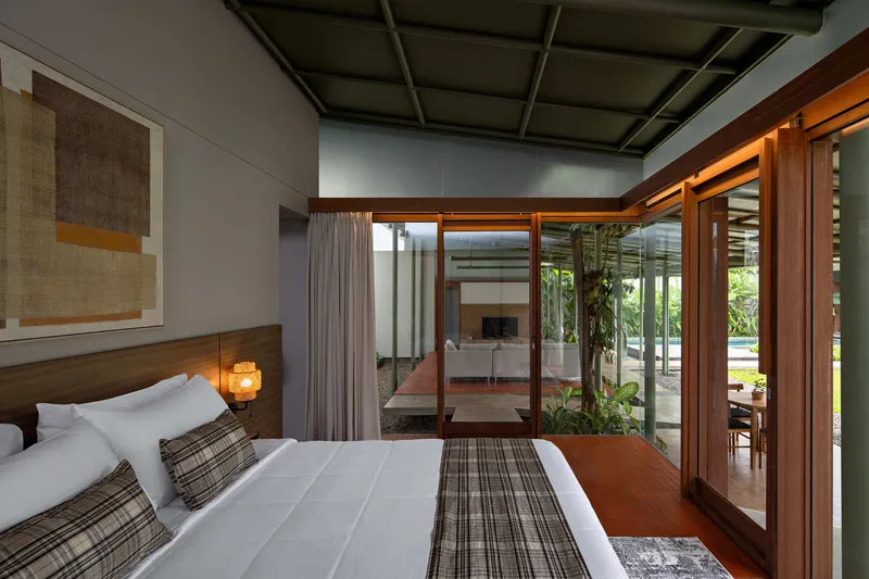 Bedroom with timber framed glazing opening onto an internal courtyard planted with tropical foliage