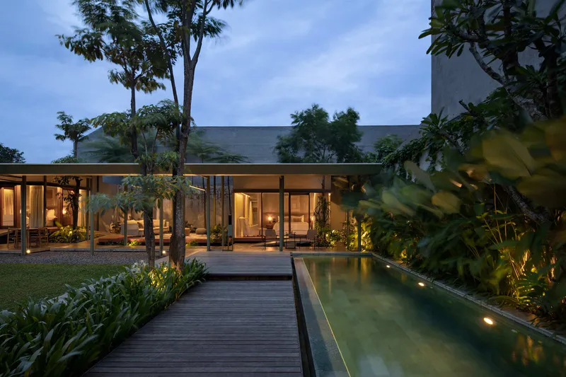 Garden view showing the lap pool with timber deck and glazed pavilion lit at twilight