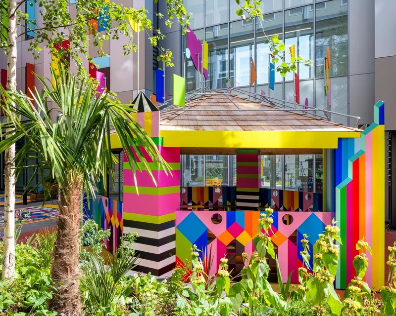 Multicolored pavilion with striped columns and patterned facade surrounded by palm trees and planted beds