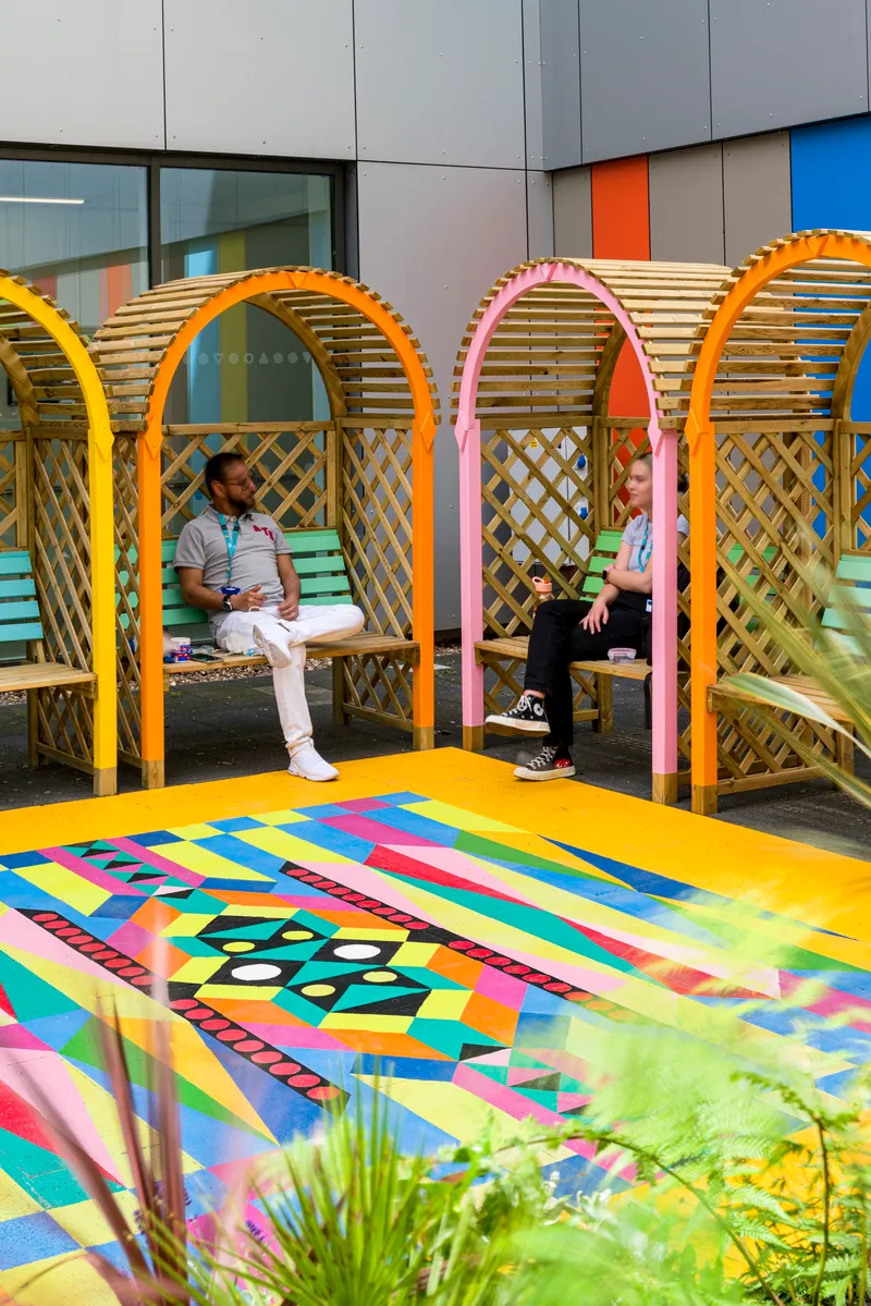 Courtyard with arched timber lattice seating alcoves and multicolored geometric paving beneath planted beds