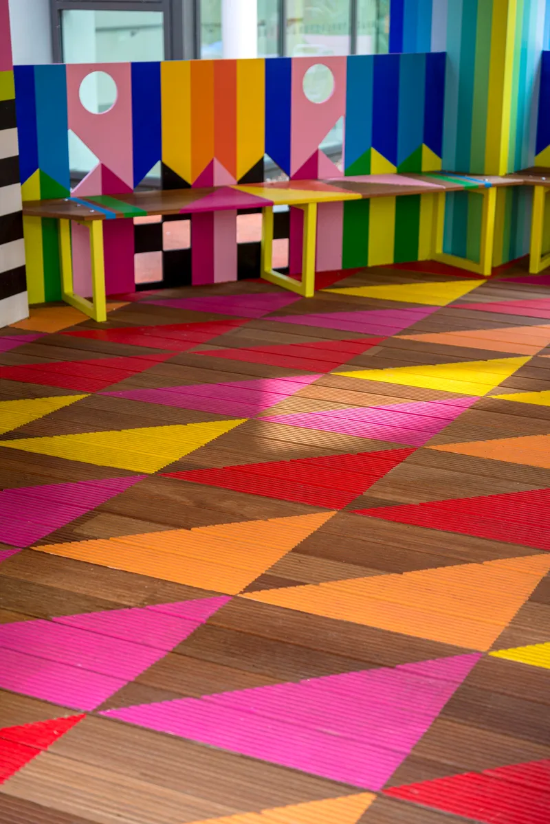 Interior timber decking with diagonal multicolored planks and benches against striped painted walls
