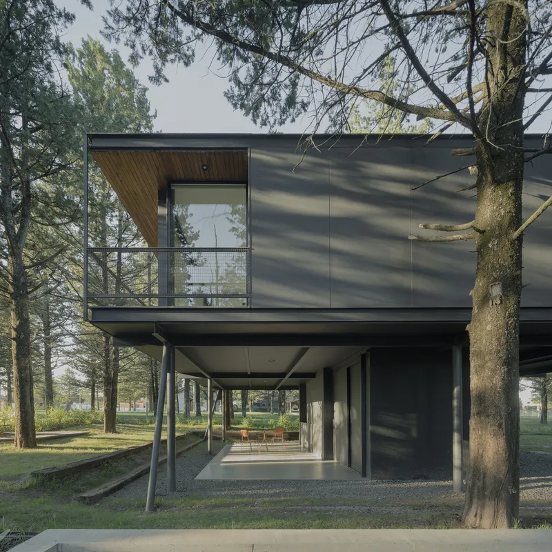 Metal-clad upper level with timber-lined balcony recess supported by slender angled columns below