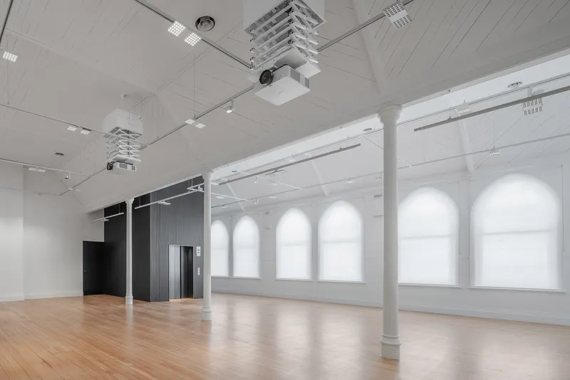 Open gallery space with timber flooring, white cylindrical columns and arched wall niches along glazed facade