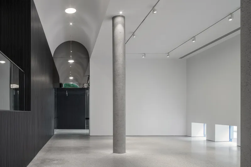 Gallery room with polished concrete floor, cylindrical grey column and low rectangular openings in white wall