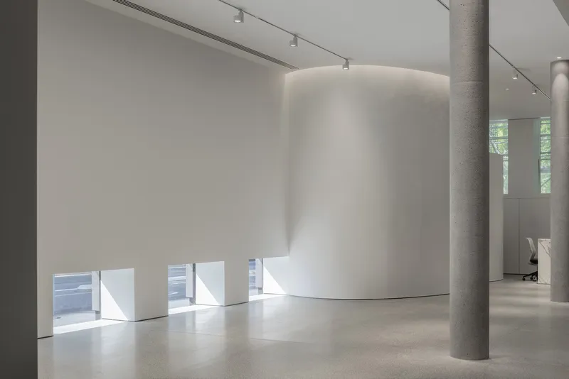Curved white plaster volume beside concrete column with horizontal window slots at floor level