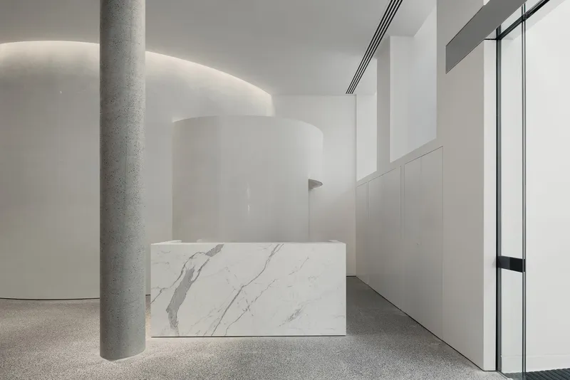 Marble reception desk with grey veining beside a terrazzo column and curved white wall with cove lighting