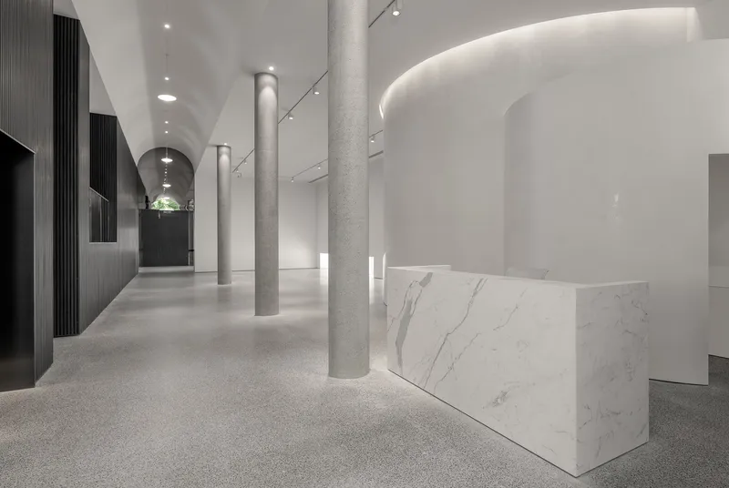 Corridor view with terrazzo columns flanking a marble reception counter and arched ceiling lit from above