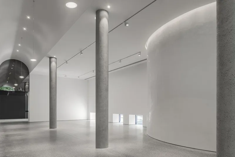 White gallery interior with cylindrical concrete columns and curved walls beneath vaulted ceiling