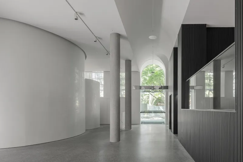 Interior corridor view through concrete columns toward arched window opening with greenery beyond