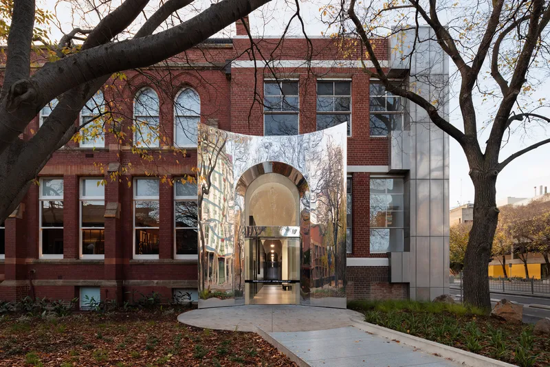 Glass and polished metal entry portal connecting red brick facades framed by bare tree branches in autumn
