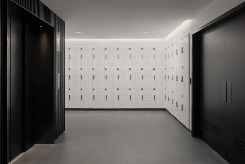 Locker room with white perforated metal lockers flanked by dark fluted wall panels and black storage units