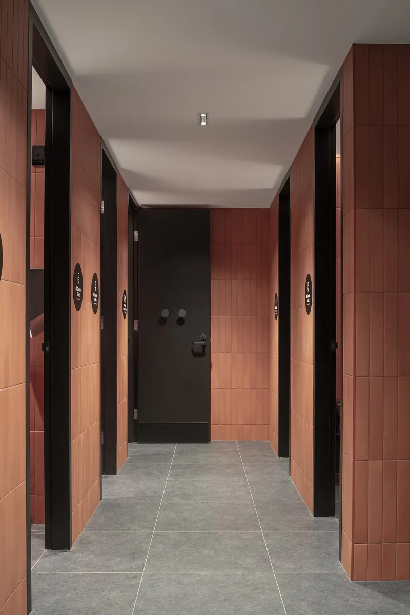 Corridor with terracotta tile walls, black-framed doors and grey stone flooring leading to a dark entry door