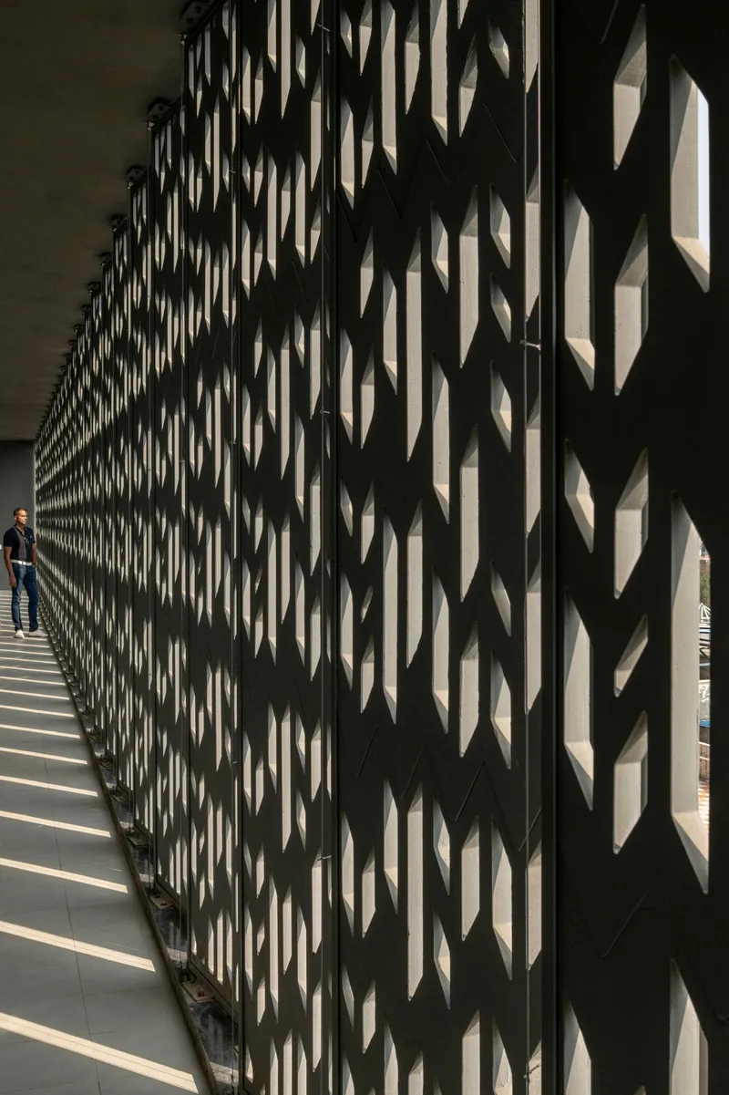 Chevron-patterned screen wall creating layered shadows along the interior walkway with a person standing