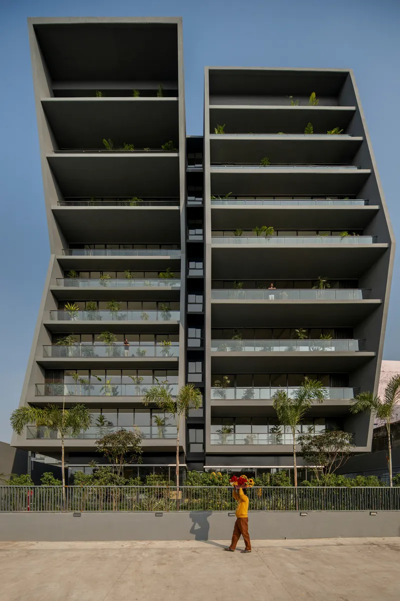 Street view of the twin angled volumes with planted terraces as a figure in orange walks past