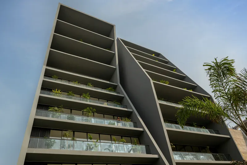 Angled view of the building facade showing horizontal balcony slabs with planted edges and palm tree in foreground