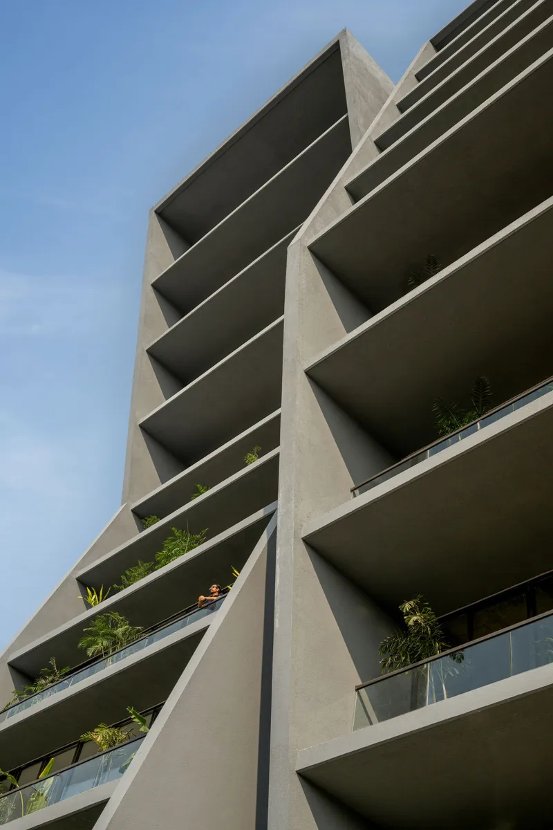 Close-up of diagonal concrete wall panels intersecting the recessed balcony floors with planted greenery