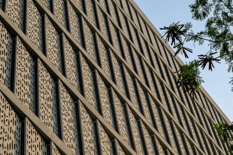 Diagonal view of the patterned brick screen wall with concrete grid framing beneath foliage