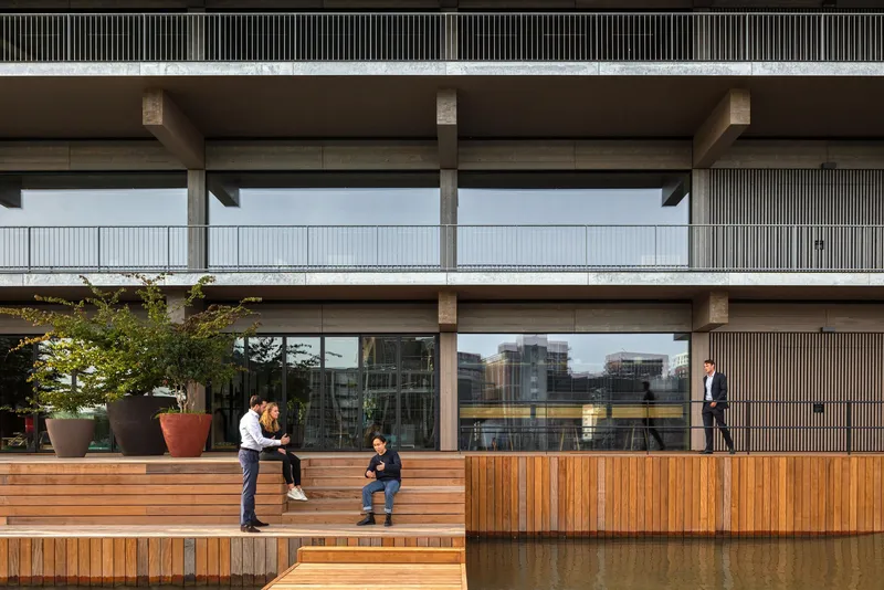 Timber deck terrace with potted tree and seated residents facing glass-walled units with vertical screening