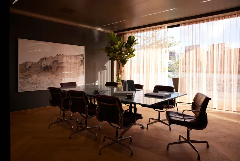 Conference room with black glass table and sheer curtains filtering daylight from floor-to-ceiling windows