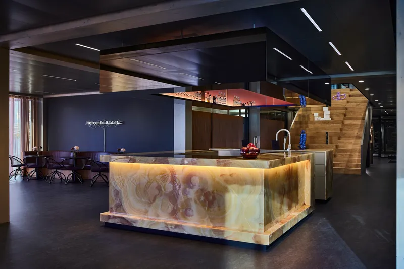 Backlit onyx kitchen island with polished veining under a black coffered ceiling