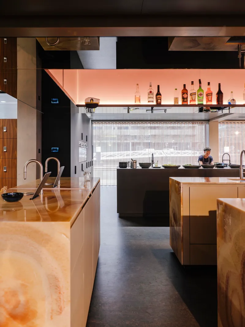 Kitchen passageway showing onyx counters and backlit bar shelving with a worker visible beyond