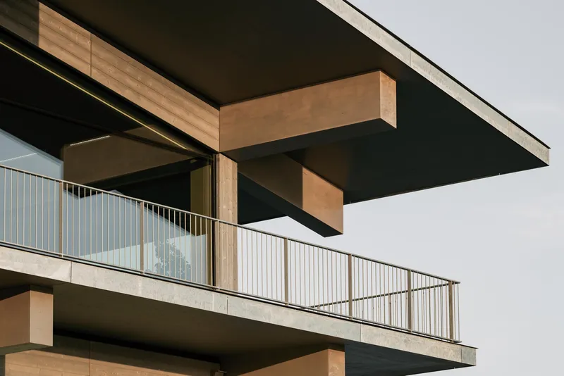 Close-up of the cantilevered balcony with timber beams and vertical metal railing under an overcast sky