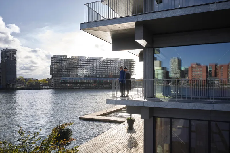 Stacked concrete balconies with metal railings overlooking the waterfront and distant buildings on a cloudy afternoon