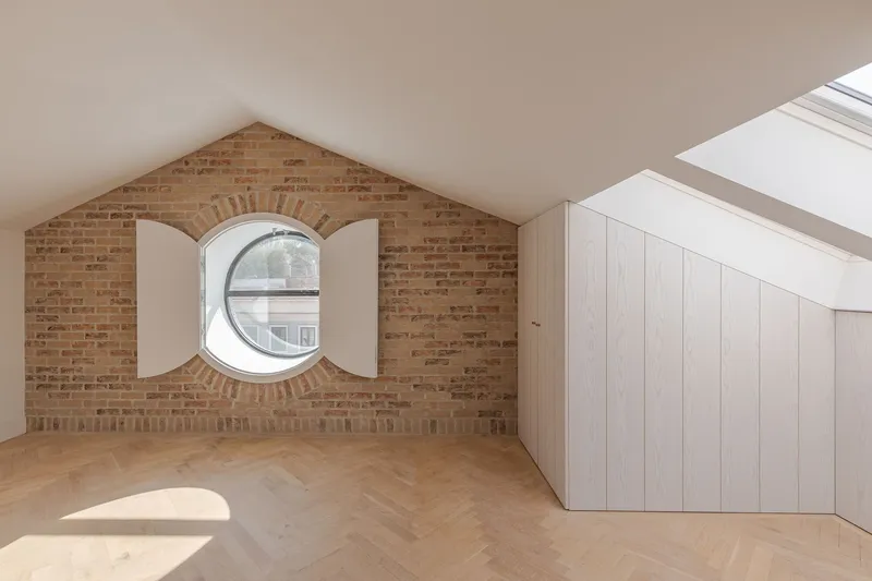 Exposed brick gable wall with circular window flanked by white shutters under the eaves