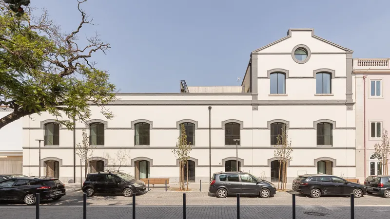 White rendered facade with arched windows and horizontal banding facing a public plaza with a mature tree