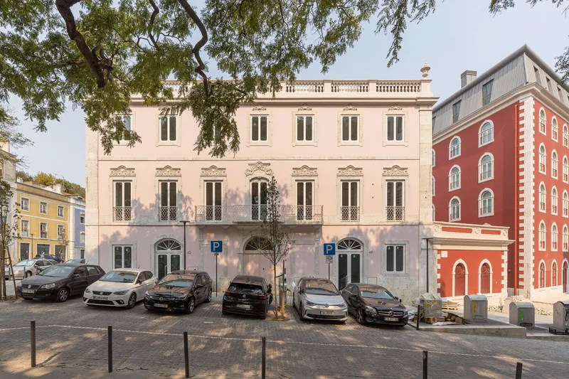 Three-story pink stucco facade with arched ground floor entrances and tree shadows in late afternoon light
