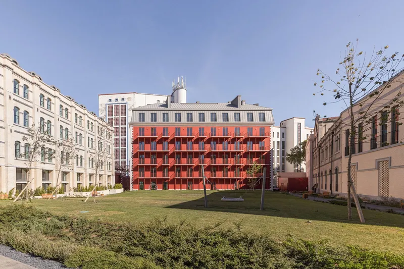 Red corrugated facade facing a central lawn courtyard framed by restored heritage buildings
