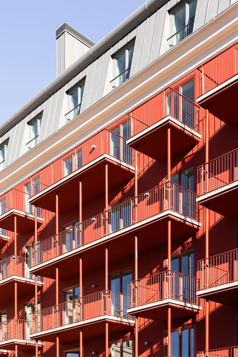 Angled red metal balconies with white trim protruding from the corrugated facade in daylight