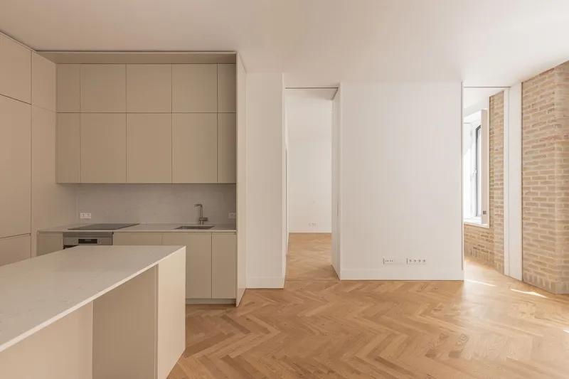 Kitchen with pale cabinetry and central island opening to herringbone floor and exposed brick wall