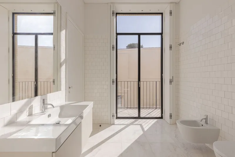 Bathroom with white subway tiles and glass door opening onto a narrow terrace with metal railing