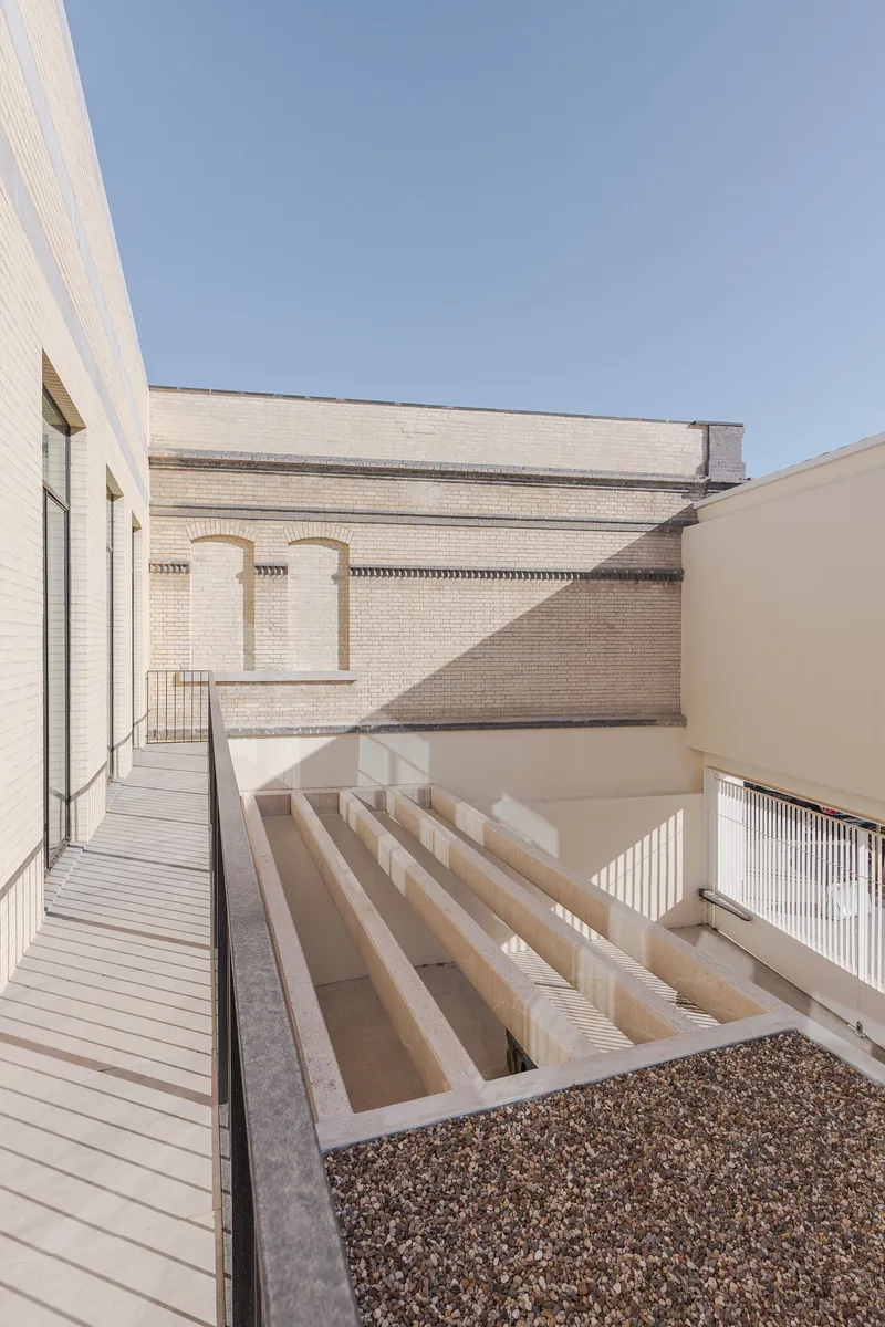 Rooftop terrace with timber decking and saw-tooth skylight structure under a clear blue sky