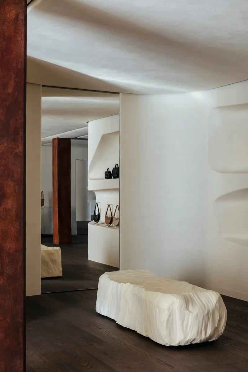 Sculpted onyx bench beneath a white plaster niche with indirect lighting and framed doorway beyond