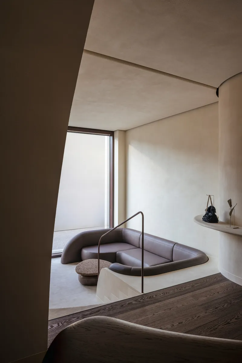 Sunken seating area with curved leather banquette beneath a tall window in soft daylight