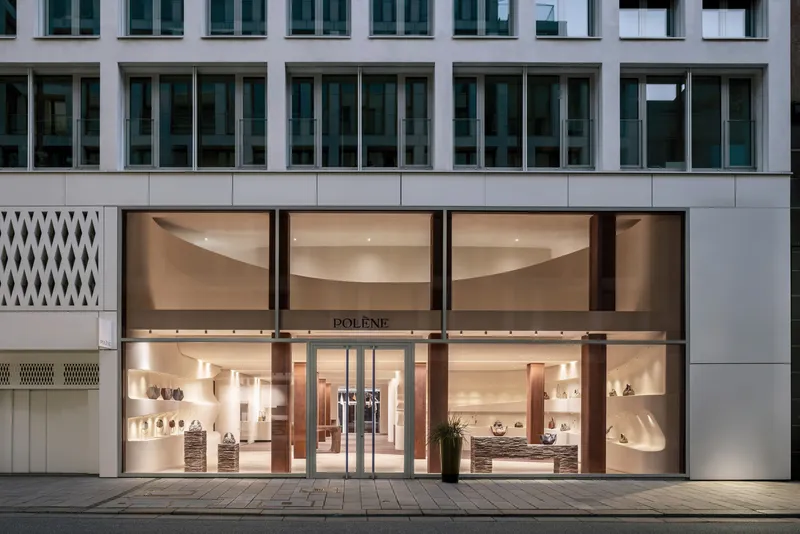 Street facade with glazed storefront revealing curved shelving and warm interior lighting at dusk