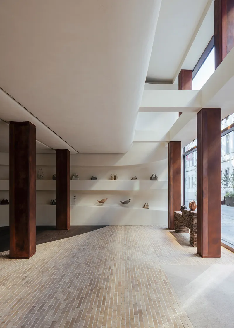 Double-height retail interior with dark timber columns, herringbone floor and floating display shelves illuminated by daylight