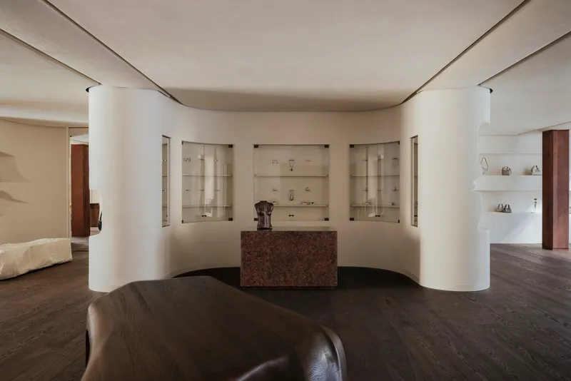 Curved wall with recessed glass vitrines flanking a central red granite counter beneath indirect cove lighting