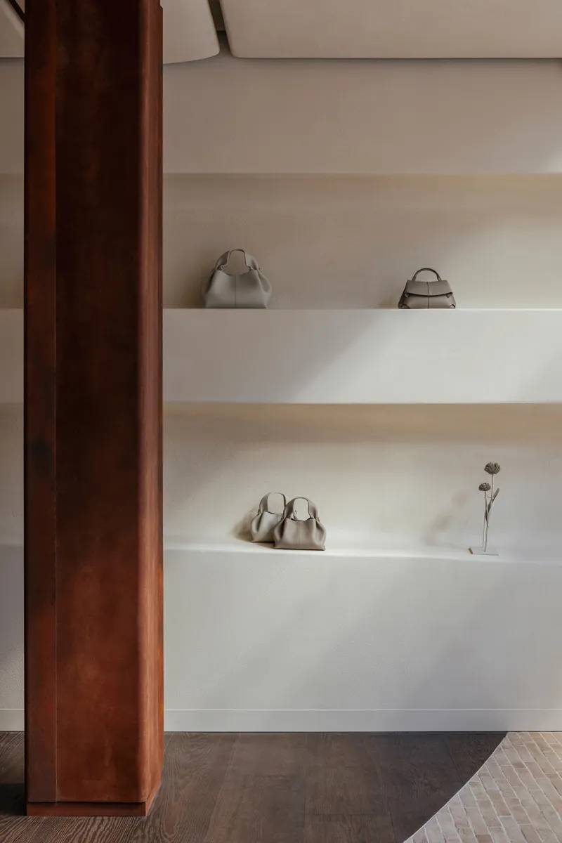 Detail of white floating shelves displaying merchandise beside a dark timber column in soft natural light