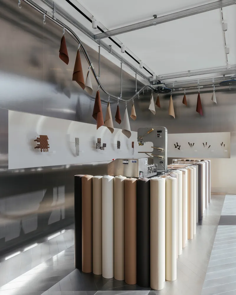 Retail space with cylindrical display table, exposed track lighting and leather samples hanging from overhead rails