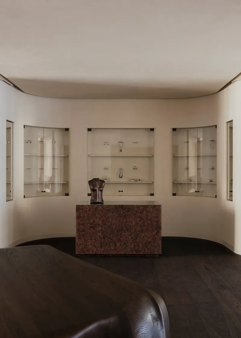 Symmetrical view of curved wall with illuminated vitrines and red granite counter on dark timber flooring