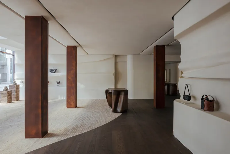 Interior retail space with weathered steel columns, curved white shelving, and dark oak flooring