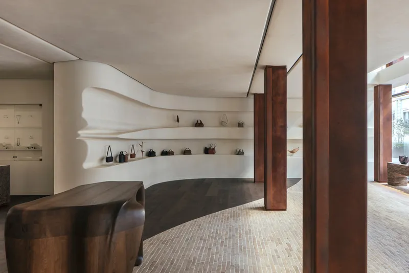 Sculpted white plaster shelving with undulating edges displaying handbags between dark timber columns