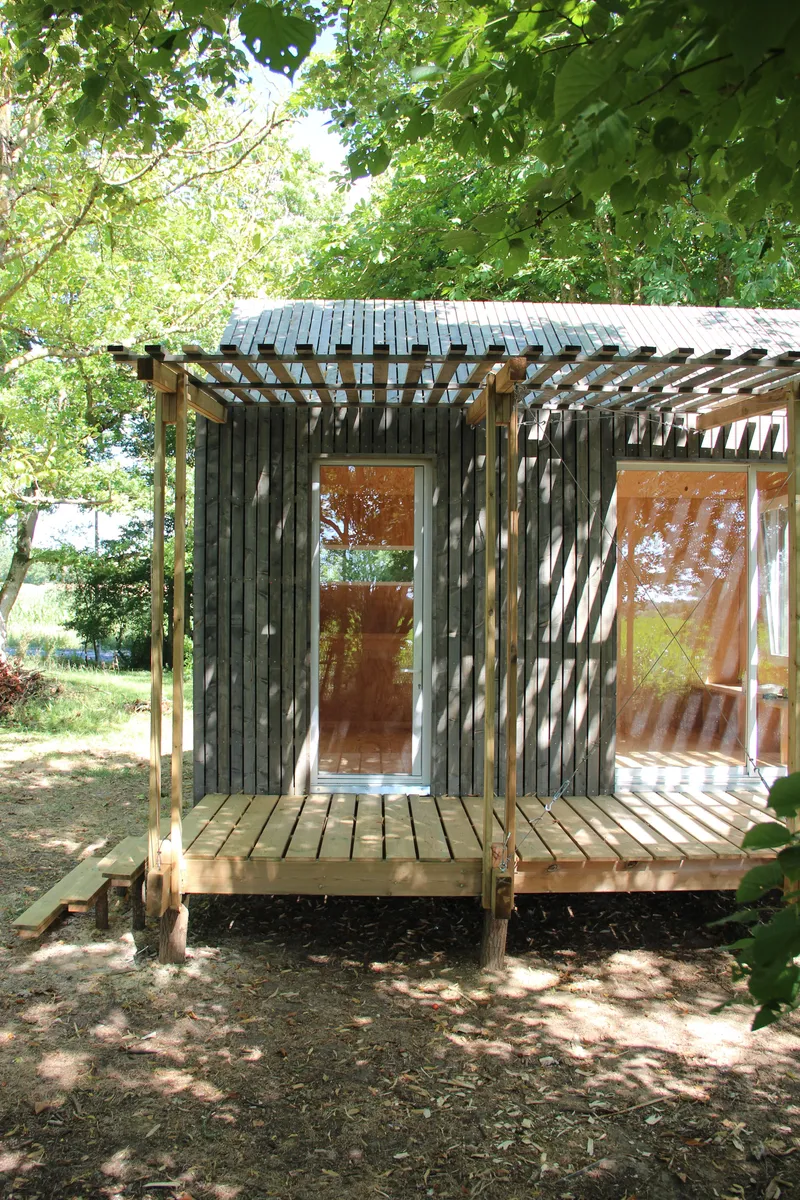 Entrance facade with timber pergola casting shadow patterns across corrugated metal walls and deck