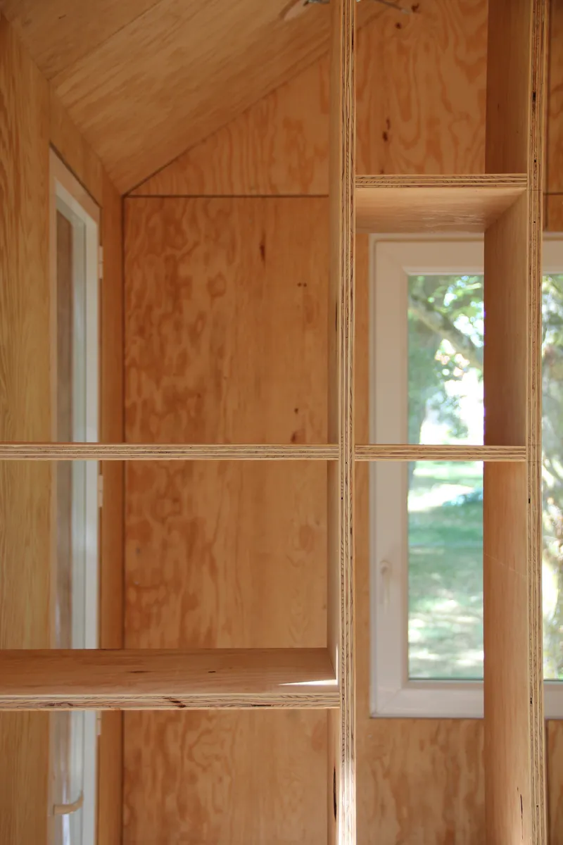 Plywood interior with built-in shelving and narrow windows overlooking green lawn in daylight