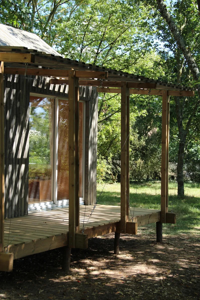 Timber-framed pavilion with exposed rafters and decking beneath dappled tree canopy