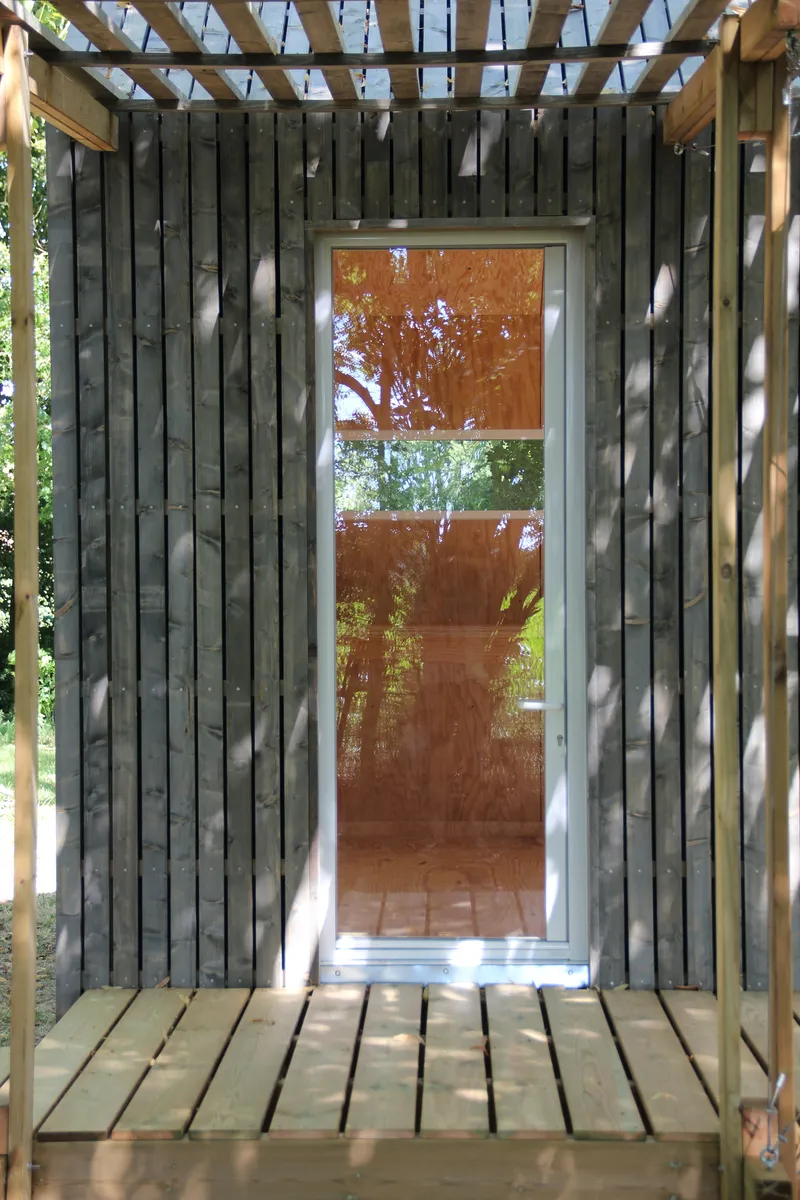 Glazed door in charred wood cladding with timber pergola casting shadows on the deck