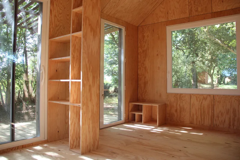 Interior plywood-lined room with built-in shelving and glazed doors opening to the deck in afternoon light